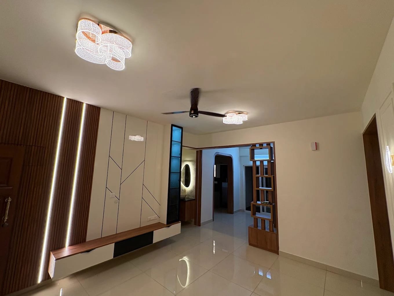Living room with fluted timber panels and vertical LED lines, a white inlaid wall panel, floating console, glass display column and open timber partition
