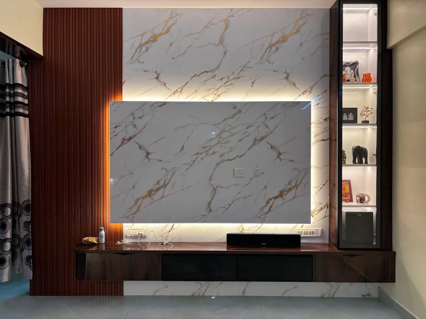 Living room TV wall with a backlit marble-finish panel, vertical fluted timber panel, floating walnut console and glass-fronted display cabinet