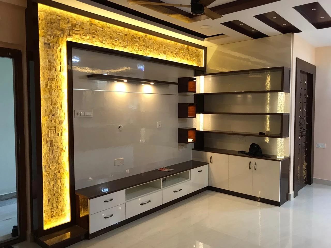 TV wall framed in backlit stone cladding with floating shelves and lit display cubes